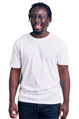 Wall Mural - Young african american man with braids wearing casual white tshirt winking looking at the camera with sexy expression, cheerful and happy face.