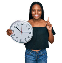 Poster - Young african american woman holding big clock surprised with an idea or question pointing finger with happy face, number one