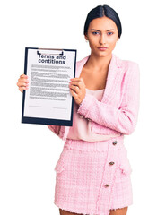 Canvas Print - Young beautiful latin girl holding clipboard with terms and conditions document thinking attitude and sober expression looking self confident