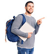© Krakenimages.com - Young handsome man wearing student backpack holding notebook smiling happy pointing with hand and finger to the side
