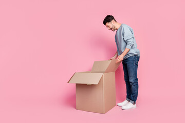 Sticker - Full length photo of attractive young man bending over peek inside carton box wear stylish blue garment isolated on pink color background