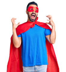 Poster - Young hispanic man wearing super hero costume crazy and mad shouting and yelling with aggressive expression and arms raised. frustration concept.