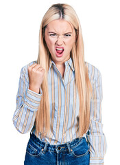 Wall Mural - Beautiful blonde woman wearing casual striped shirt angry and mad raising fist frustrated and furious while shouting with anger. rage and aggressive concept.