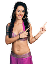 Young Indian Woman Wearing Belly Dancer Costume Smiling And Looking At The Camera Pointing With Two Hands And Fingers To The Side.