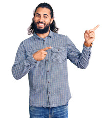 Young arab man wearing casual clothes smiling and looking at the camera pointing with two hands and fingers to the side.