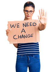 Poster - Young beautiful woman holding we need a change banner with open hand doing stop sign with serious and confident expression, defense gesture