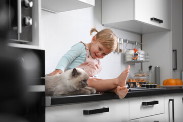 Poster - Cute little child sitting with adorable pet on countertop in kitchen