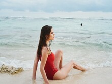 A Woman With Wet Hair Sits On The Sand With Slender, Tanned Legs On An Ocean Beach In Bali And Looks Out At The Horizon, The Concept Of Traveling The World And Vacationing In Islands