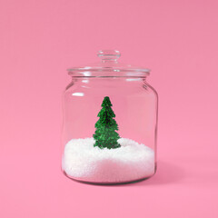 Wall Mural - Christmas tree with snow in a glass jar on pastel pink background. Creative winter background. Flat lay, top view.