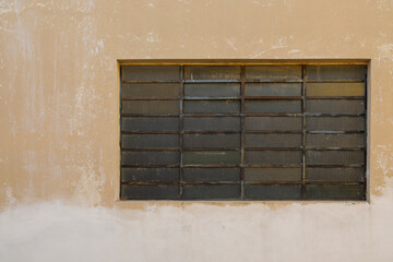 Yellow painted house wall with glass brick stones as a window, frame rusty and weathered, background with space