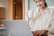© mungkornz - businesswoman working on laptop in the morning on the bed with hot coffee.