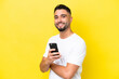 © luismolinero - Young Arab handsome man isolated on yellow background holding a mobile phone and with arms crossed