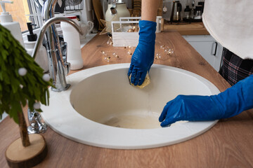 Cleaning sink in kitchen before the Christmas and New Year holidays. Hand in gloves and sponge, detergent, dry powder. Festive decor in the white kitchen, cozy interior of the home