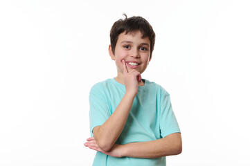 Happy multi-ethnic child boy wearing blue t-shirt, holding his hand at chin and cutely smiling, thoughtfully looking at camera, isolated over white background with copy ad space for promotional text