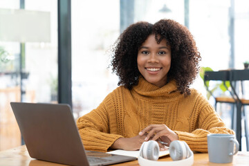 Photo of cheerful joyful mixed-race woman in yellow shirt smiling work on laptop talk speak video call online. Smart ethnic female in earphones study distant on computer at home. Education concept.