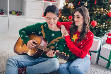 Canvas Print - Portrait of two peaceful partners sit carpet floor cuddle play acoustic guitar newyear decoration house indoors