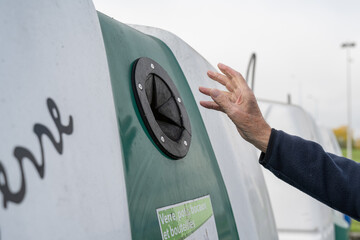 main d'un homme jetant une bouteille dans une benne de recyclage