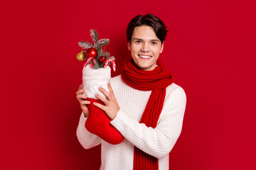 Canvas Print - Photo of young smile brunet hair student guy wear fall season scarf hold xmas sock adornment baubles preparation isolated on red color background