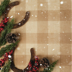 Wall Mural - Western industry Christmas background with snow over horseshoes on rustic plaid, copy space for holiday.