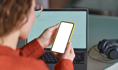 Over shoulder view of woman holding mobile phone with white blank mock up cellular screen applications working using cell phone. Cellphone display mock up for advertising apps concept.