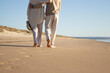 Romantic couple enjoying vacation at seaside while walking along beach and embracing. Back view of middle-aged man and woman spending holiday time together. Coastline background. Love, leisure concept