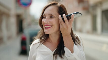 Wall Mural - Young beautiful hispanic woman smiling confident listening audio message by the smartphone at street