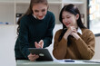 © NanSan - Cheerful asian business woman wearing sweater with colleagues working together at workplace female office worker during working day in office, looking at tablet