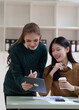 © NanSan - Cheerful asian business woman wearing sweater with colleagues working together at workplace female office worker during working day in office, looking at tablet