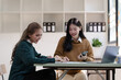 © NanSan - Cheerful asian business woman wearing sweater with colleagues working together at workplace female office worker during working day in office, pointing chart paper