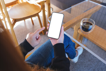 Top view mockup image of a woman holding and touching on mobile phone with blank desktop screen with coffee cup on the table