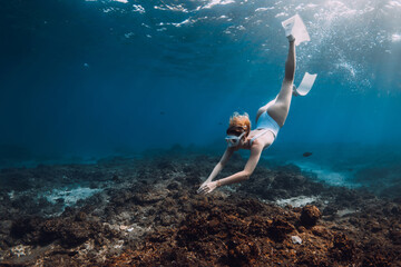 Wall Mural - Woman freediver in white swim wear dive with fins over corals. Freediving in tropical blue ocean