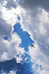 Wall Mural - The passenger airplane is flying far away in the blue sky. Dramatic clouds with the sun shining through them. Aircraft in the air. Vertical illustration. Passenger air transportation