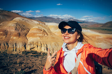 Cheerful woman tourist take a selfie with amazing mountain view. Happy young brunette enjoying vacation. Female traveller portrait.