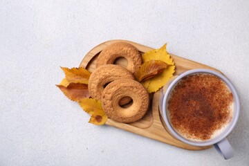 Wall Mural - Cup of hot drink, cookies and autumn leaves on light grey textured table, top view. Space for text