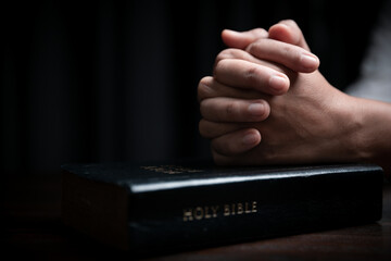 Faith with holy bible concept. Hands of a female prayer worship God with holy bible on black background in church. Christian woman who believe in Jesus read and study the grace of the holy scriptures.