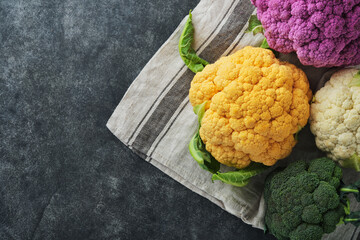 Colorfu cauliflower. Various sort of cauliflower on old dark gray concrete background. Purple, yellow, white and green color cabbages. Broccoli and Romanesco. Agricultural harvest. Mock up.