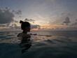 © Anastasiia - Girl in an outdoor rooftop pool with the ocean in the background looking out into the distance. Beautiful slender woman swimming in the water of a luxurious pool at night after sunset.