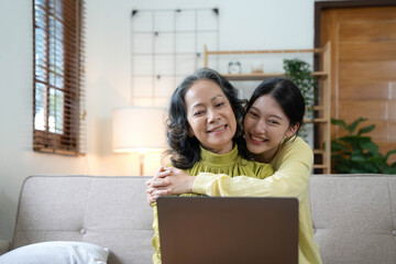 Wall Mural - Happy adult granddaughter and senior grandmother having fun enjoying talk sit on sofa in modern living room, smiling old mother hugging young grown daughter bonding chatting relaxing at home together