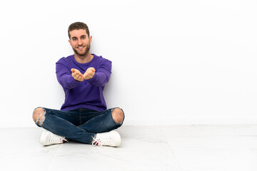 Poster - Young man sitting on the floor holding copyspace imaginary on the palm to insert an ad