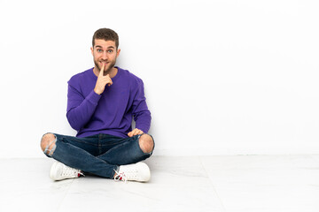 Poster - Young man sitting on the floor showing a sign of silence gesture putting finger in mouth