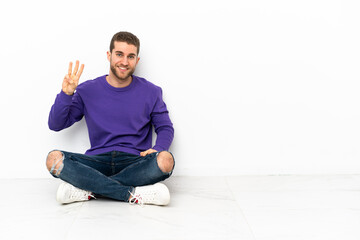 Canvas Print - Young man sitting on the floor happy and counting three with fingers