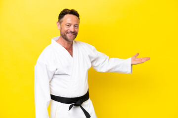 Middle age caucasian man doing karate isolated on yellow background extending hands to the side for inviting to come