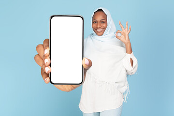 Excited black muslim woman showing phone blank screen and gesturing okay, space for website or app design, mockup