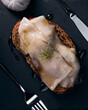 una fetta di pane, o bruschettta, con fette di lardo sopra e rosmarino, impiattata con coltello forchetta e un filo di olio
