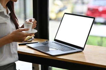 Poster - Cropped image with Empty screen of laptop and Business woman's hand holding a cup of coffee, Coffee break.