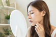 © KMPZZZ - Dermatology, puberty asian young woman, girl looking into mirror, allergy when wear mask and cosmetic, show squeezing pimple spot for removing from face.Beauty care from skin problem by acne treatment