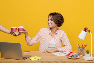 Poster - Young smiling employee business woman wearing shirt take takeaway paper cup coffee to go sit work at office desk with pc laptop isolated on plain yellow color background. Achievement career concept.