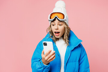 Snowboarder amazed woman wear blue suit goggles mask hat ski padded jacket hold use mobile cell phone isolated on plain pastel pink background. Winter extreme sport hobby weekend trip relax concept.