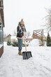 Close-up of a woman cleaning and clearing snow in front of the house on a sunny and frosty day. Cleaning the street from snow on a winter day. Snowfall, and a severe snowstorm in winter.
