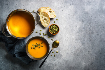 Wall Mural - Pumpkin soup in the pot and in black bowl at stone table. Top view with copy space.